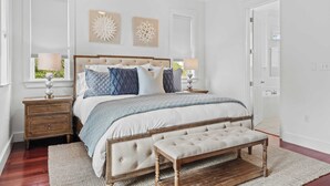 Un dormitorio con una cama grande, un banco de madera, dos mesitas de noche y decoración en la pared.
