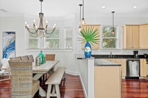 A modern kitchen with wooden cabinets, a stainless steel dishwasher, and a dining area with wicker furniture. - Dragonfly Dreams 30A by Avantstay Walk to Beach (Panama City Beach)
