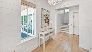 Un hall d’entrée spacieux, avec des lambris blancs, un lustre, un escalier et une grande fenêtre offrant une belle vue.