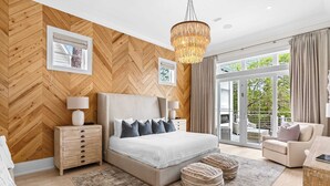 Een slaapkamer met een groot bed, houten lambrisering, een kroonluchter, een nachtkastje, een lamp, een raam en uitzicht op de omgeving.