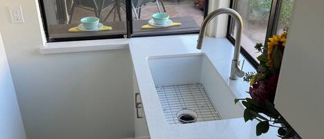 A compact kitchen with a sink, a window overlooking a patio with outdoor furniture, and a decorative wall piece.