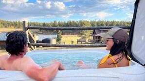 A couple relaxing in a hot tub with a view of a rural landscape.