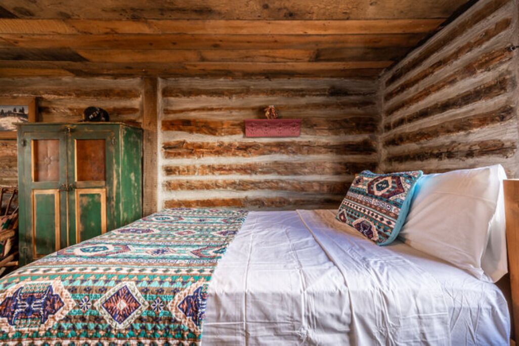 A rustic wooden cabin room with a bed, a green cabinet, and a patterned rug.