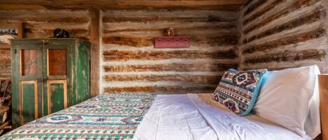 A rustic wooden cabin room with a bed, a green cabinet, and a patterned rug.