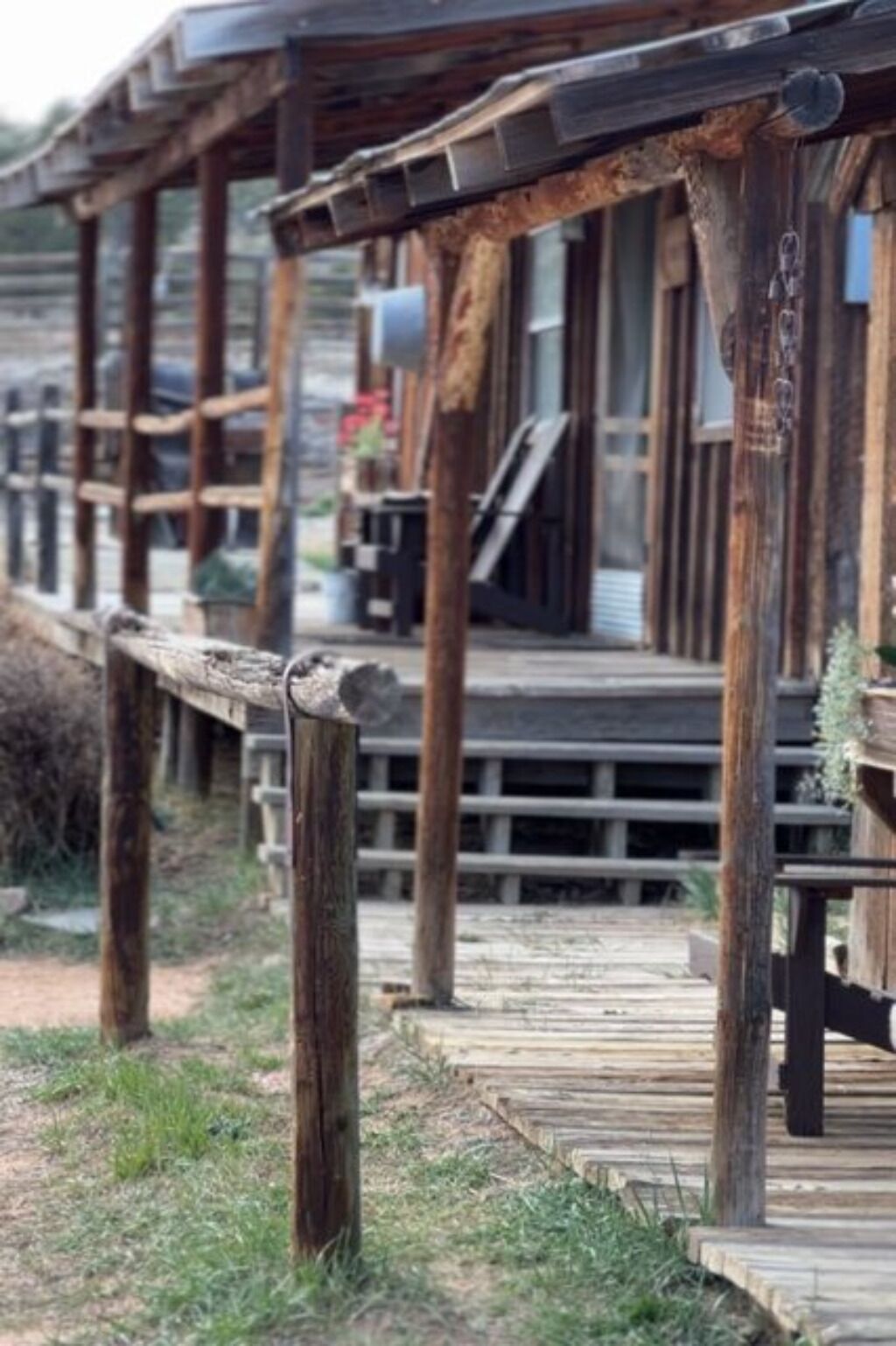 A rustic wooden deck with a wooden railing, leading to a building with a sloped roof and a window.