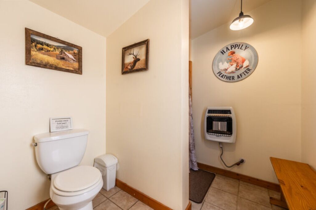 A bathroom with a toilet, a trash can, a wall-mounted heater, and two framed pictures.