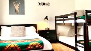 A bedroom with a bunk bed, a single bed, a ceiling fan, a wall-mounted lamp, and a framed deer head artwork. - Prospector Cabin - Kitchen included (Lake George)