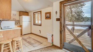 A compact kitchen with a refrigerator, wooden cabinets, a microwave, and a window with blinds. - Prospector Cabin - Kitchen included (Lake George)
