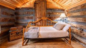 A log cabin bedroom with a wooden bed, a nightstand, a lamp, and a suitcase. - Rustler Cabin - Kitchen  included (Lake George)