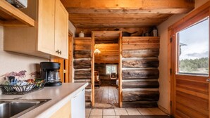A log cabin kitchen with wooden cabinets, a coffee maker, and a view through an open doorway. - Rustler Cabin - Kitchen  included (Lake George)
