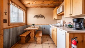A compact kitchen with wooden cabinets, a wooden table, a bench, a microwave, a coffee maker, and a fire extinguisher. - Rustler Cabin - Kitchen  included (Lake George)