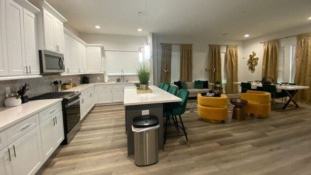 Une cuisine moderne avec des meubles blancs, un îlot central et un coin repas agrémenté de poufs jaunes et de chaises vertes.
