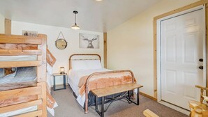 Un dormitorio con una cama de madera, un banco, una mesita de noche con lámpara y una puerta.