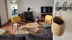 A cozy living room with a fireplace, a sofa, a television, and a wicker basket. - Tipoz'Immo • Maison Bleue Walking distance to the beach • Surf spot • garden (Pouldreuzic)