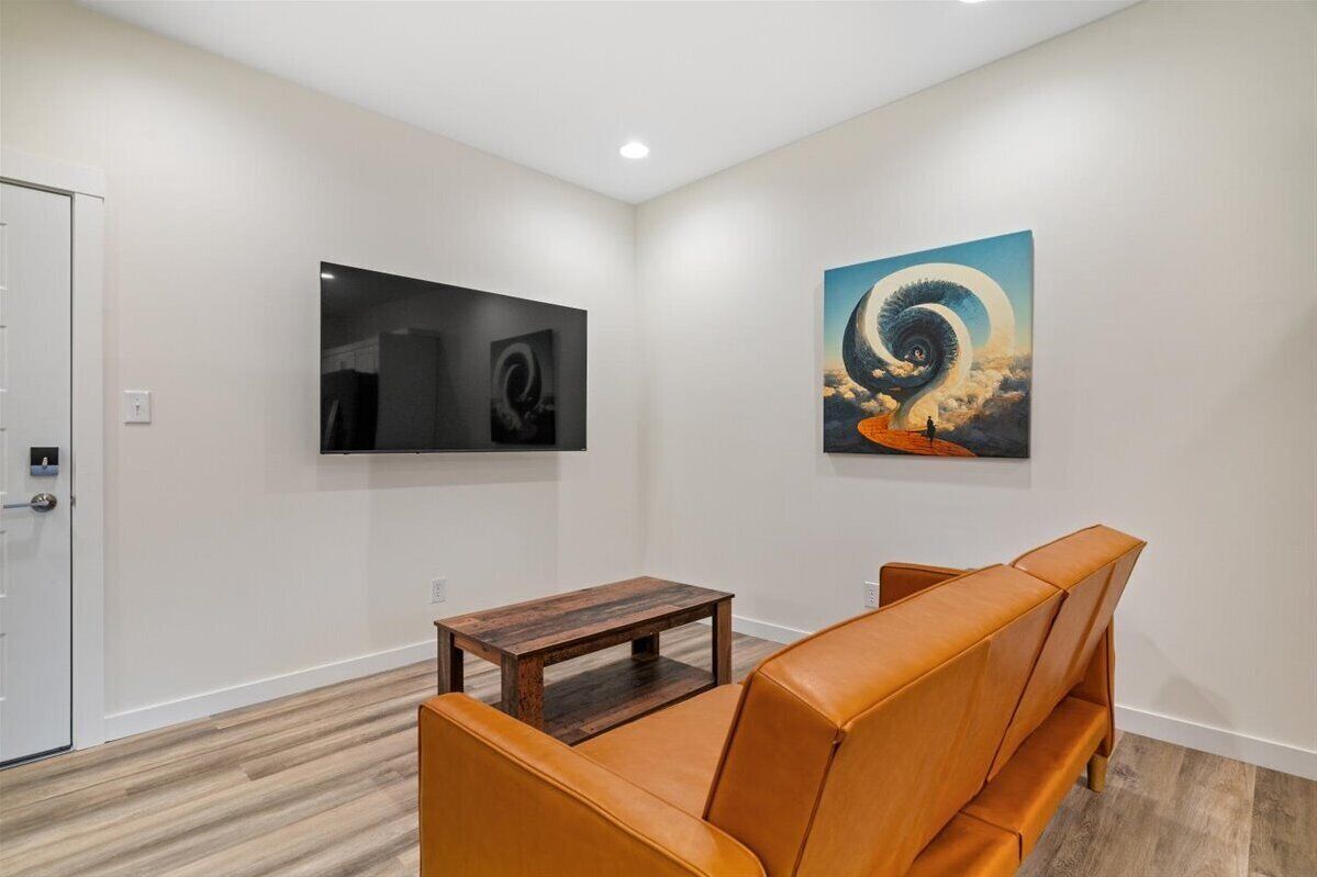 A modern living room with a brown leather sofa, a wooden coffee table, and two framed artworks on the walls.