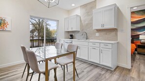 A modern kitchen with white cabinets, a glass dining table, and a large window.