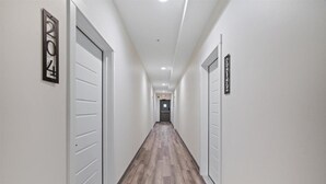 A hallway with white walls, wooden flooring, and closed doors on both sides.