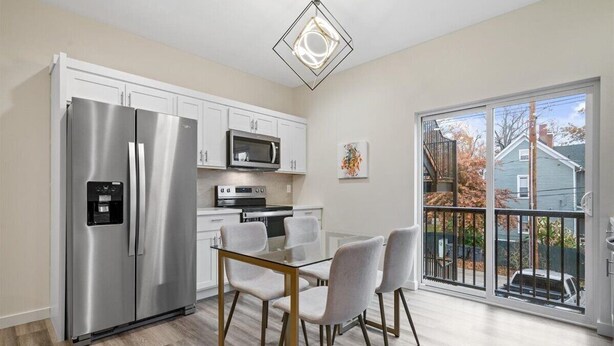 A modern kitchen with stainless steel appliances, a glass dining table, and a view of the outside through large sliding glass doors.