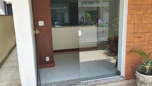 Une porte vitrée donne accès à un bâtiment dont le sol est recouvert de carreaux et devant lequel se trouve un pot de fleurs.
