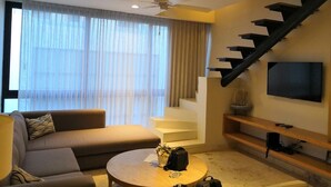 A modern living room with a sofa, a round coffee table, a TV mounted on the wall, and a staircase with a unique design. - Amazing 2 floor penthouse w/PRIVATE rooftop (Playa del Carmen)
