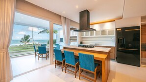 Een moderne keuken met een groot eiland, een eethoek met blauwe stoelen en uitzicht op zee.