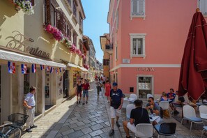 Une rue étroite bordée de terrasses, de boutiques et de balcons ornés de fleurs.