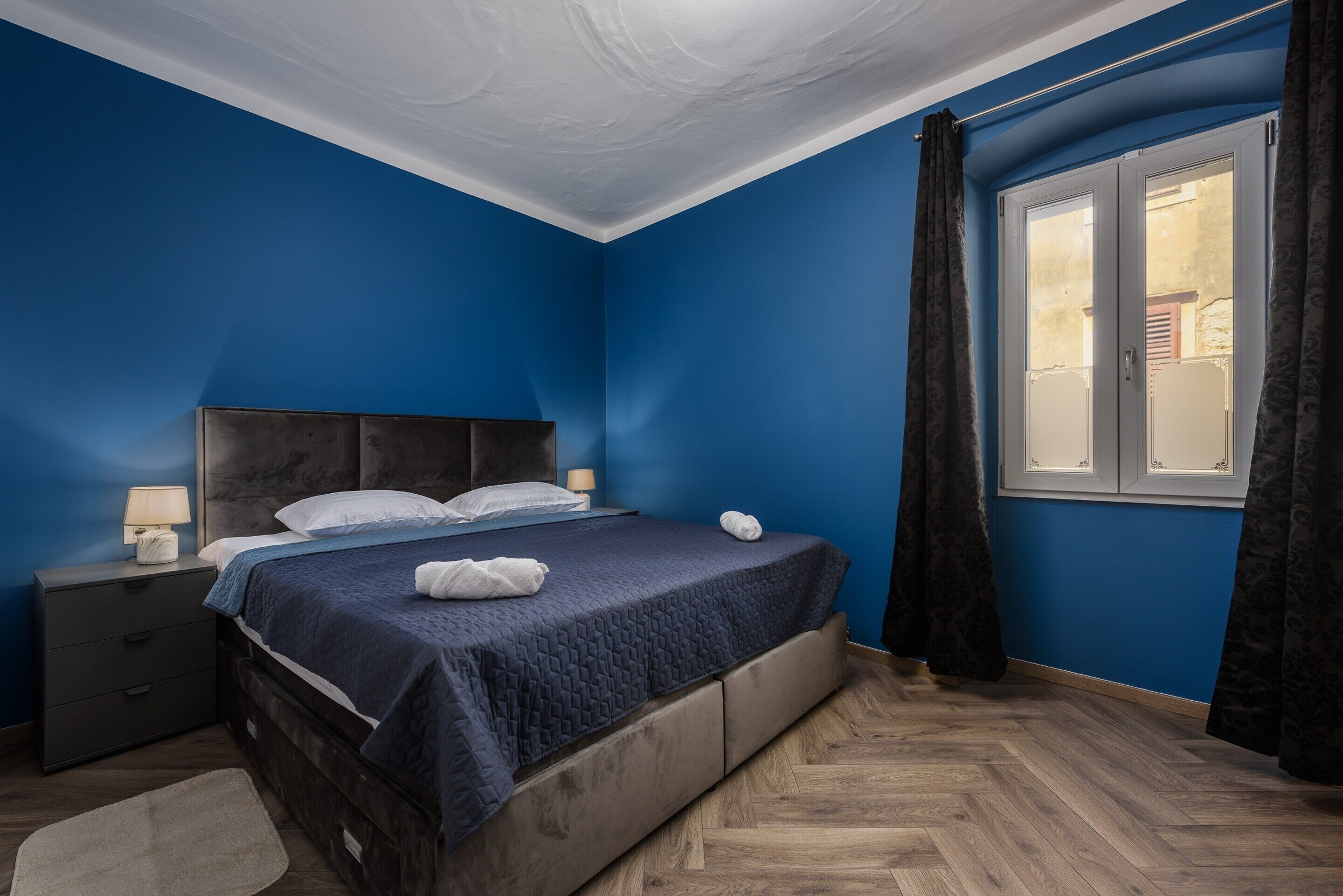 Une chambre à coucher avec un lit, une table de chevet et une fenêtre avec des rideaux.