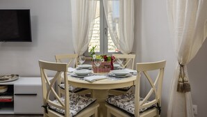 Een eetruimte met een ronde tafel gedekt voor vier personen, omringd door vier stoelen met gestreepte kussens. Op de tafel staat een mand met bloemen en een rode lint.