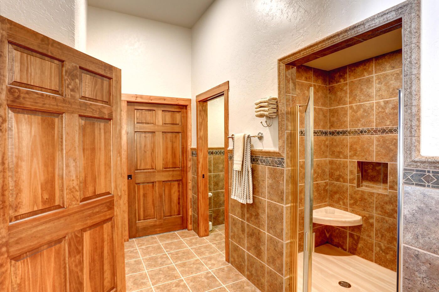 A bathroom with wooden doors, a shower with a glass door, and tiled walls.