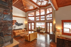 A spacious living room with a stone wall, wooden ceiling, and large windows offering a view of the outdoors.