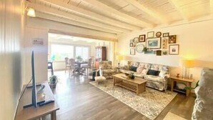 Un ampio soggiorno con soffitto in legno, un divano, un tavolino da caffè e, sullo sfondo, una zona pranzo.