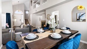 A spacious living area with a dining table set for four, a staircase, and a fireplace. - Modern 4BR Getaway w/ Pool (North Las Vegas)