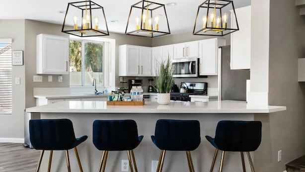 A modern kitchen with white cabinets, a central island, bar stools, and pendant lighting. - Modern 4BR Getaway w/ Pool (North Las Vegas)