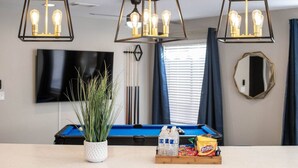 A pool table with a white pot of plants, bottled water, and snacks on a table. - Modern 4BR Getaway w/ Pool (North Las Vegas)