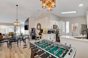 Een moderne keuken met een tafelvoetbaltafel, witte kastjes en een eethoek met een tafel en stoelen.
