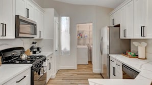 A modern kitchen with white cabinets, a stove, microwave, and refrigerator. - 4BR Family Getaway w/Pool (North Las Vegas)