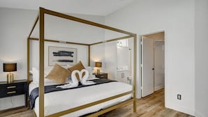 A four-poster bed with a gold frame, a nightstand with a lamp, a painting on the wall, and a door leading to another room. - 4BR Family Getaway w/Pool (North Las Vegas)