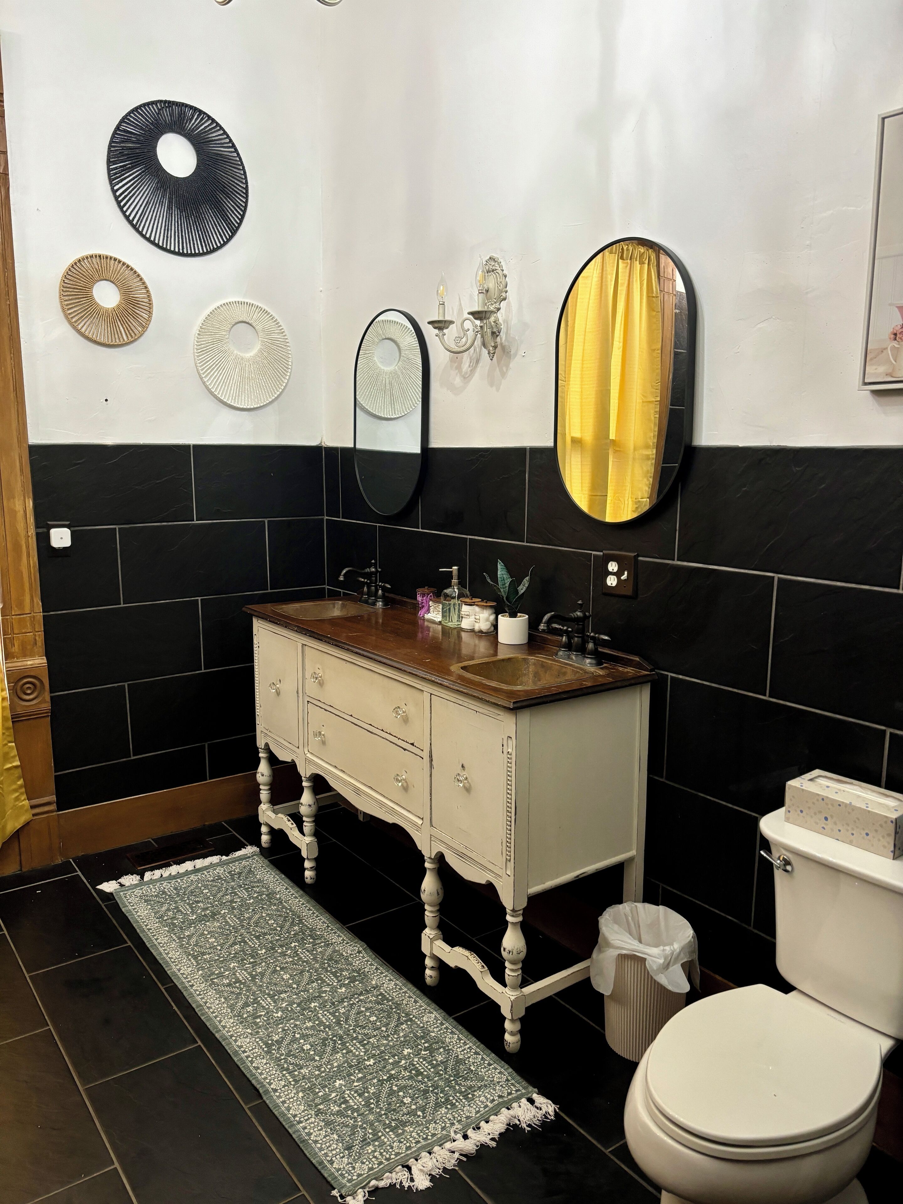 A bathroom with a white sink, black and white tiled walls, a mirror, and a yellow curtain.