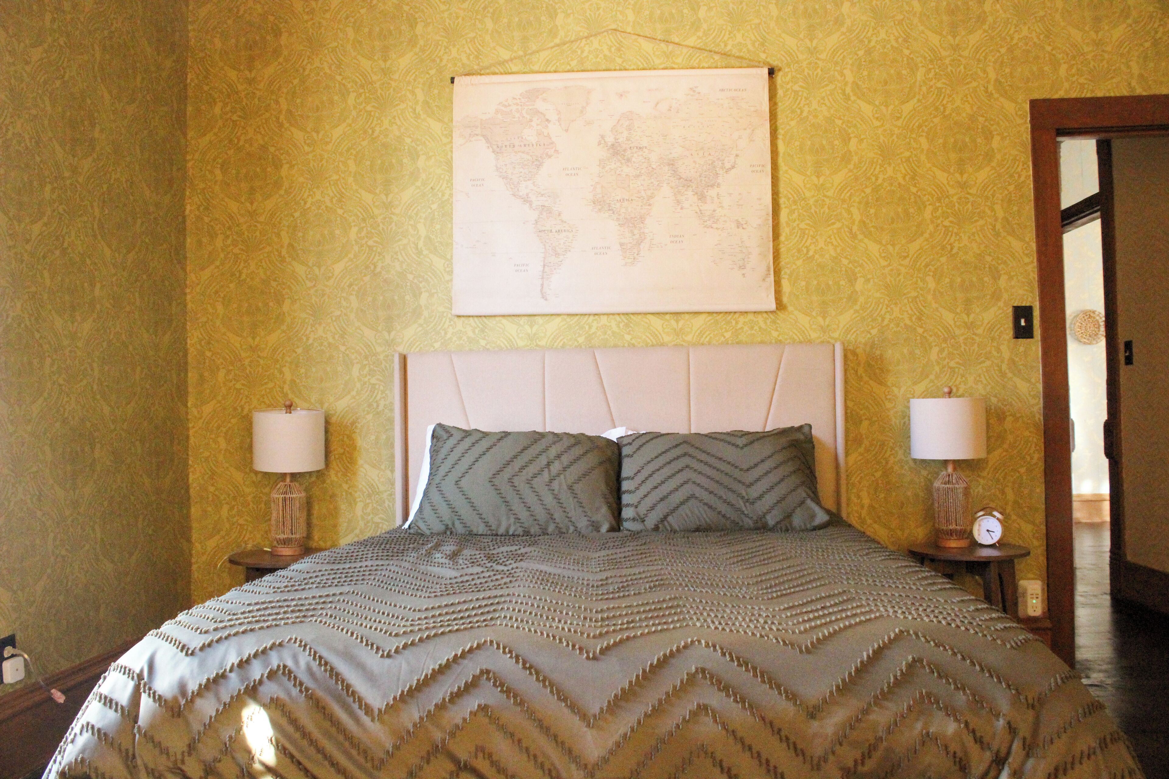 Un lit bien fait, recouvert d’une couvre-lit à motifs, avec deux oreillers, deux lampes de chevet et une carte du monde accrochée au mur.