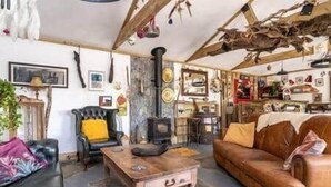 A rustic living room with a fireplace, a sofa, a wooden table, and a chair. - The Hideaway - Shore House (Muff)