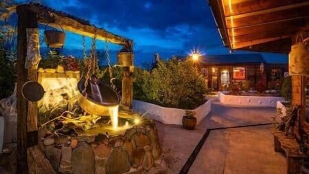 A rustic outdoor area with a stone fountain, wooden structures, and a building in the background. - The Hideaway - Shore House (Muff)