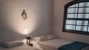 Een slaapkamer met twee bedden, een raam met zonwering, een wandlamp en een decoratief object.