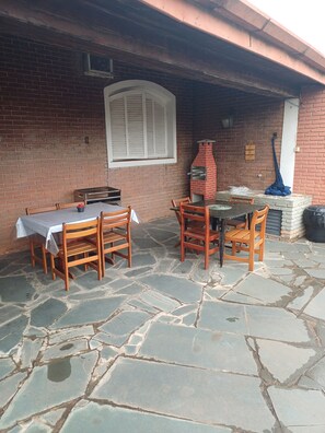 Un patio al aire libre con pared de ladrillo, piso de piedra, una mesa con sillas y un horno de ladrillo.