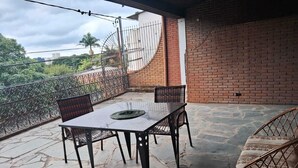 Een terras met een tafel en stoelen, een rieten stoel, een bakstenen muur en een metalen hek.