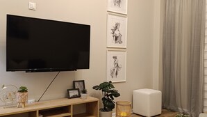 Ett modernt vardagsrum med en platt-TV, ett träinrett mediaskåp, inramade konstverk, krukväxter och ett dekorativt bricka.