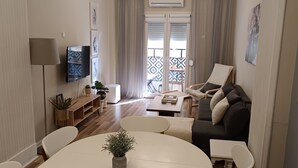 Ett modernt vardagsrum med ett runt matbord, vita stolar, en soffa och en tv.