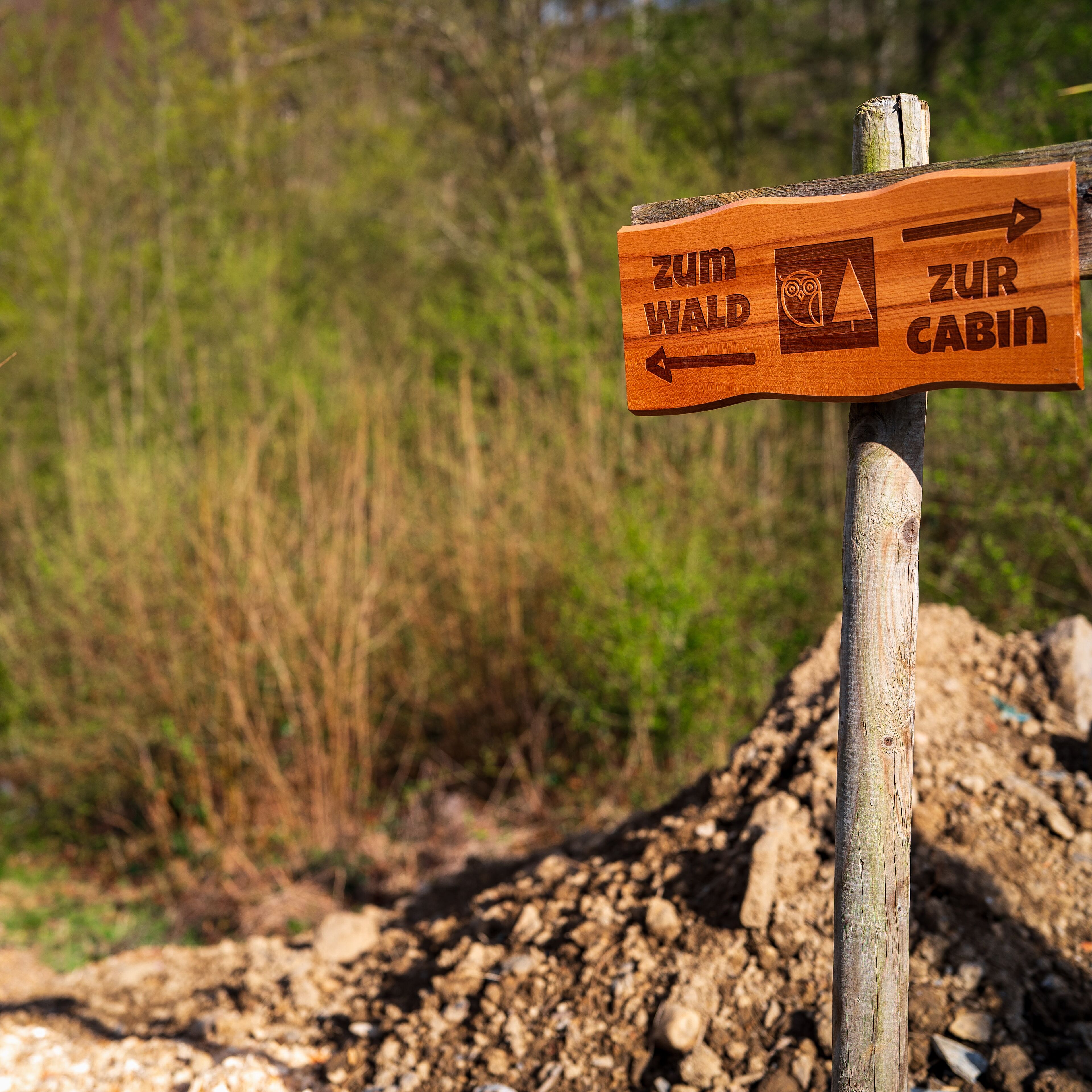 Un panneau indicateur en bois, avec des flèches pointant vers « Zum Wald » et « Zur Cabin ».