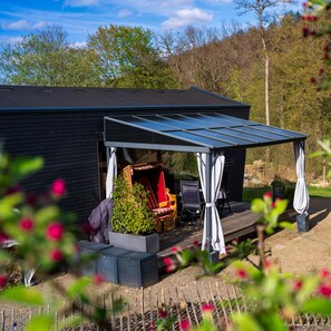 Eine moderne Außenpatio mit überdachter Sitzgruppe, einem Feuerkorb und einem Garten.