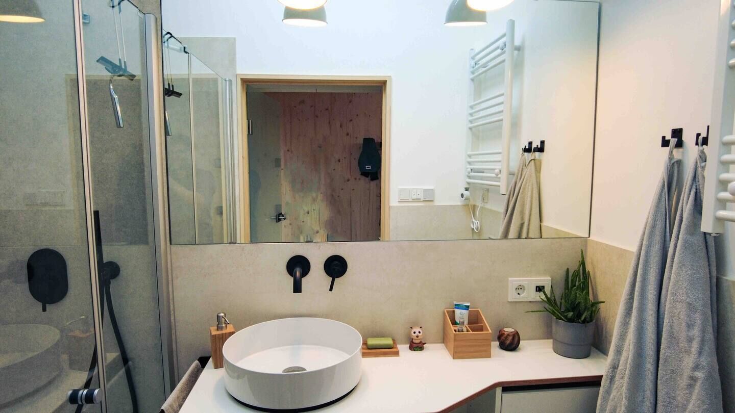 Un baño moderno con un espejo grande, un lavabo redondo, una ducha y un perchero para toallas.