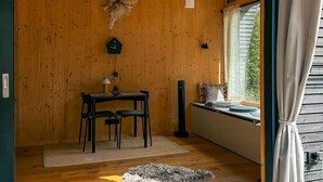A cozy room with wooden walls, a dining table with chairs, a small rug, and a window with curtains.
